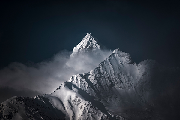 Fotobehang Natuur Besneeuwde bergtop in de wolken